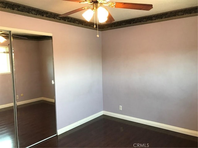 empty room with a ceiling fan, dark wood-type flooring, and baseboards