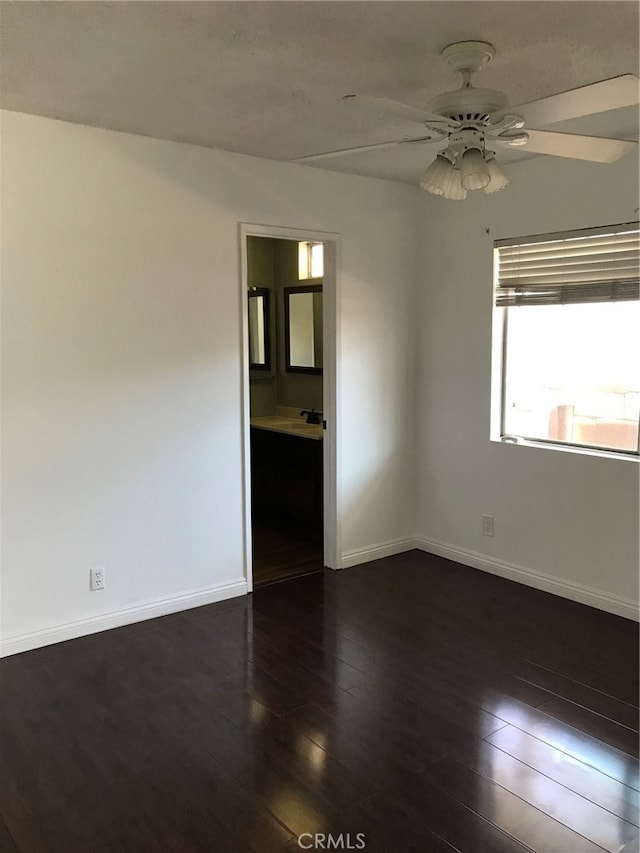 spare room featuring a ceiling fan, dark wood-type flooring, and baseboards