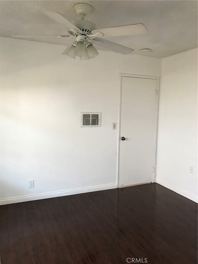 spare room with dark wood-style floors, visible vents, baseboards, and ceiling fan