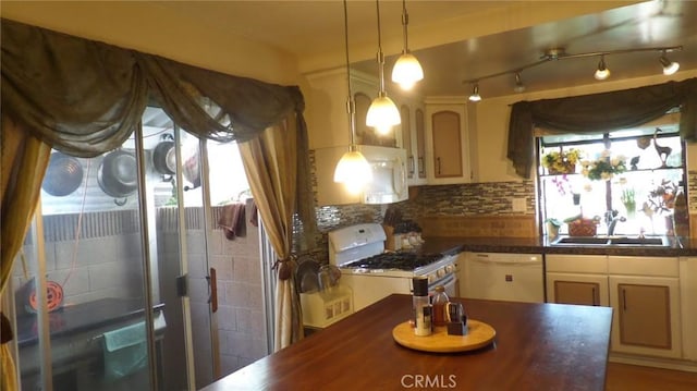 kitchen featuring white appliances, a sink, hanging light fixtures, dark countertops, and tasteful backsplash