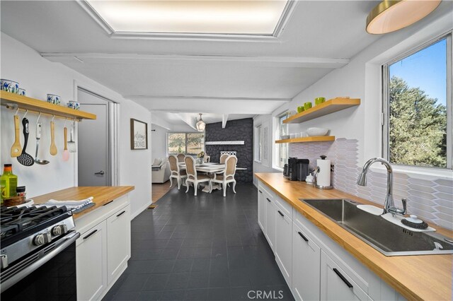 kitchen featuring white cabinets, butcher block countertops, beamed ceiling, gas range, and sink