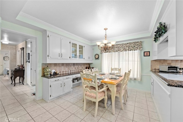 tiled dining area with ornamental molding, a raised ceiling, and a chandelier