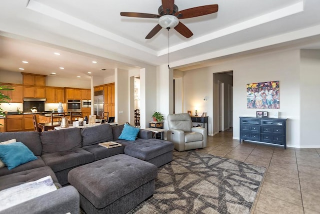 living room with a raised ceiling, dark tile patterned flooring, and ceiling fan