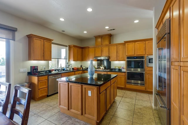 kitchen with a center island, sink, built in appliances, dark stone counters, and light tile patterned floors