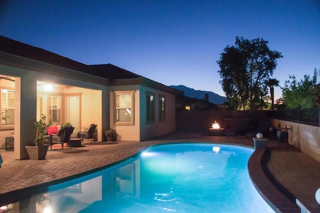 pool at dusk featuring a mountain view, a patio, and an outdoor fire pit