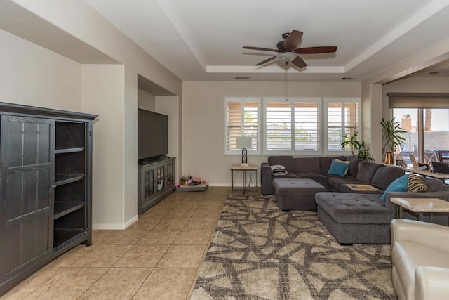 tiled living room with a tray ceiling and ceiling fan