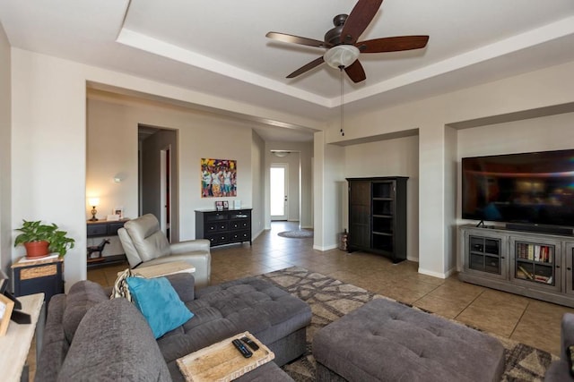 living room featuring tile patterned flooring, ceiling fan, and a raised ceiling