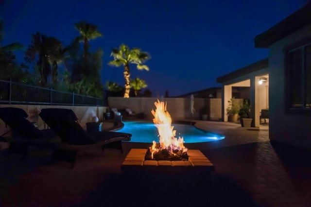 pool at night with a fire pit and a patio area