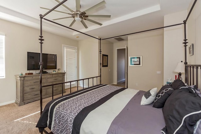 bedroom featuring multiple windows, light colored carpet, ceiling fan, and a tray ceiling