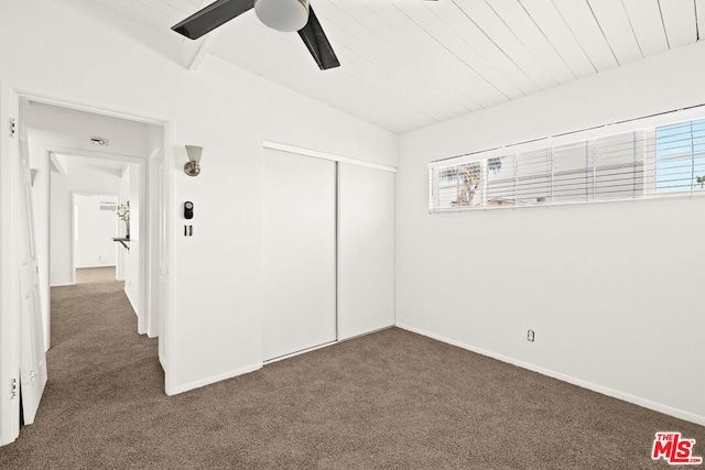 unfurnished bedroom with ceiling fan, a closet, dark colored carpet, and multiple windows