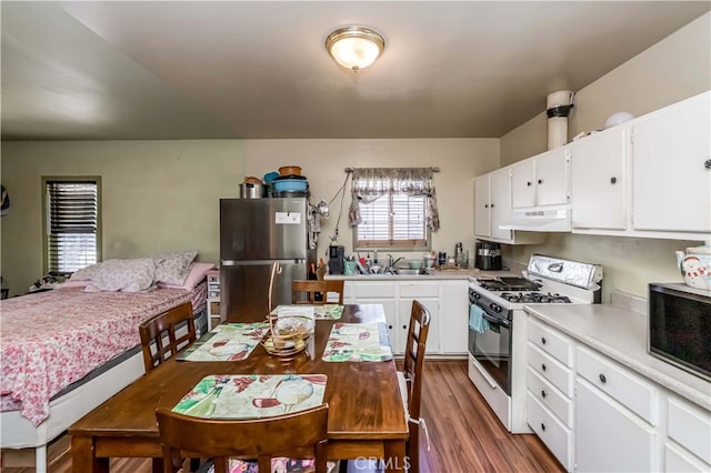 kitchen with dark wood-type flooring, white gas range oven, white cabinets, stainless steel refrigerator, and sink