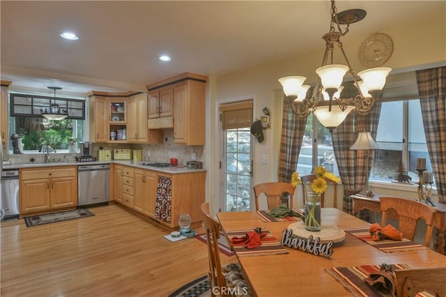 kitchen featuring decorative backsplash, stainless steel dishwasher, light hardwood / wood-style floors, and hanging light fixtures