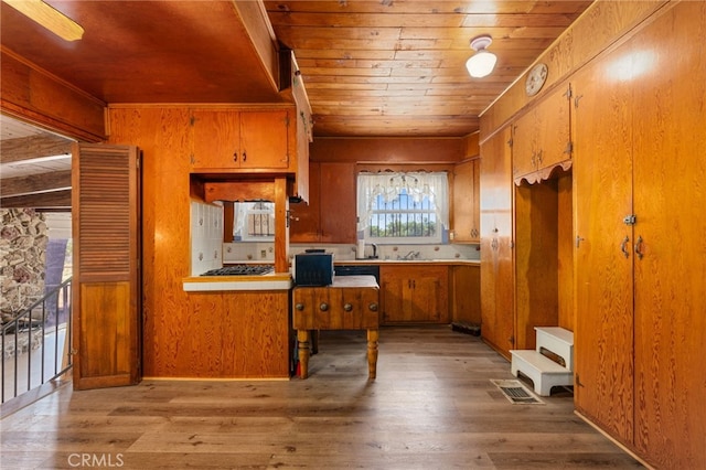 kitchen with stainless steel gas stovetop, wood ceiling, wood walls, light wood-type flooring, and sink