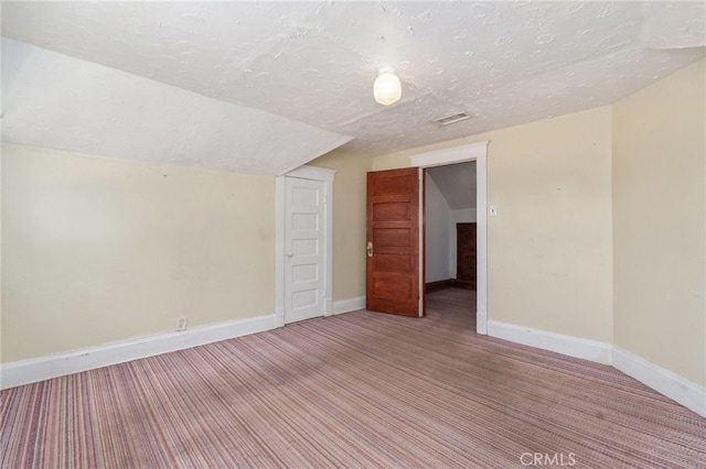 additional living space featuring vaulted ceiling, carpet, and a textured ceiling