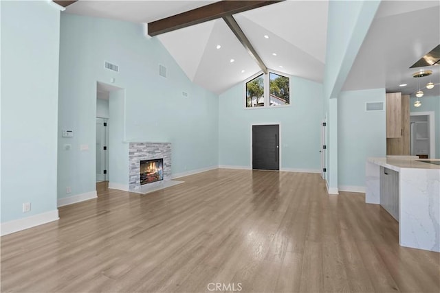 unfurnished living room with a fireplace, beamed ceiling, light hardwood / wood-style floors, and high vaulted ceiling