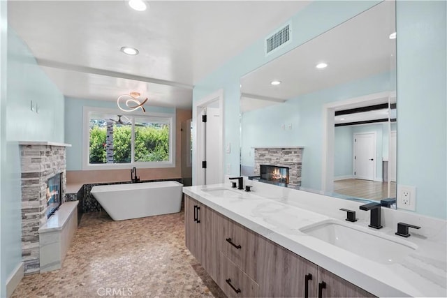 bathroom featuring a washtub, a stone fireplace, and vanity