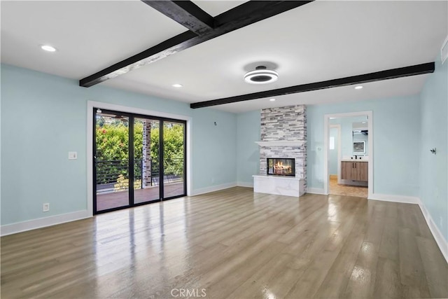 unfurnished living room featuring beam ceiling, a fireplace, and light wood-type flooring