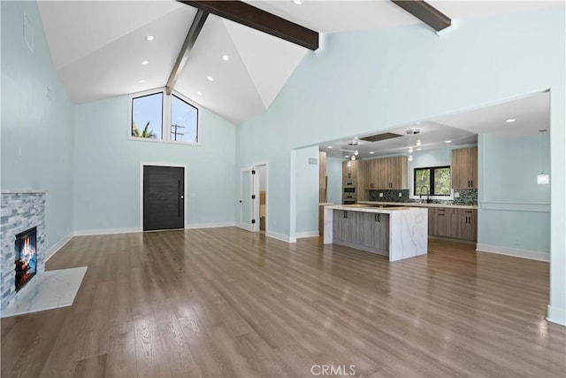 unfurnished living room with high vaulted ceiling, sink, a fireplace, beamed ceiling, and light hardwood / wood-style floors