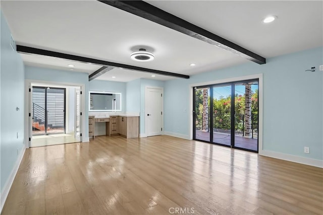 unfurnished living room featuring beamed ceiling and light wood-type flooring