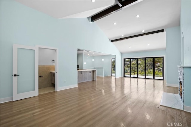 unfurnished living room with beamed ceiling, high vaulted ceiling, wood-type flooring, and french doors