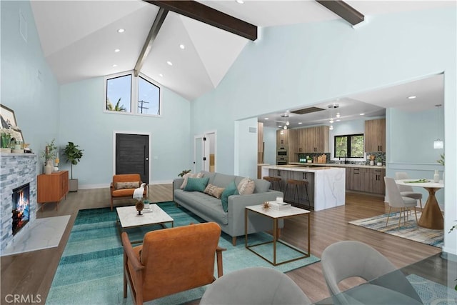 living room featuring sink, light hardwood / wood-style flooring, high vaulted ceiling, beamed ceiling, and a fireplace