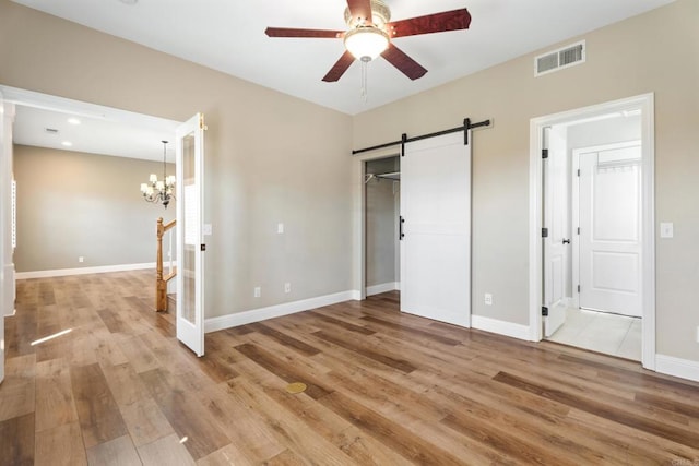 unfurnished bedroom with a barn door, light hardwood / wood-style floors, and ceiling fan with notable chandelier