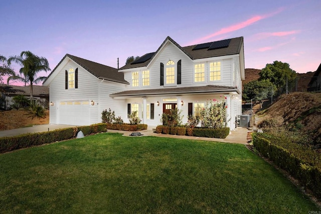 view of front facade featuring solar panels, a yard, a garage, and central AC unit