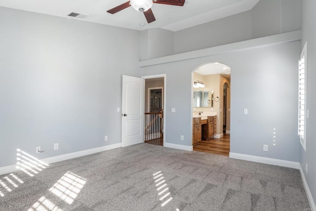 unfurnished bedroom with ensuite bathroom, carpet flooring, ceiling fan, a towering ceiling, and multiple windows