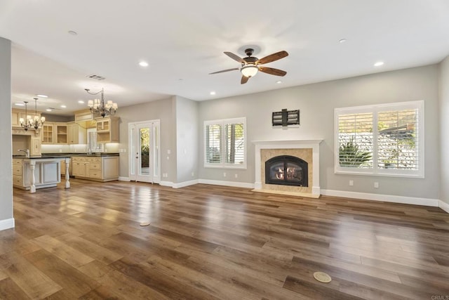 unfurnished living room featuring a wealth of natural light, ceiling fan with notable chandelier, and dark hardwood / wood-style floors