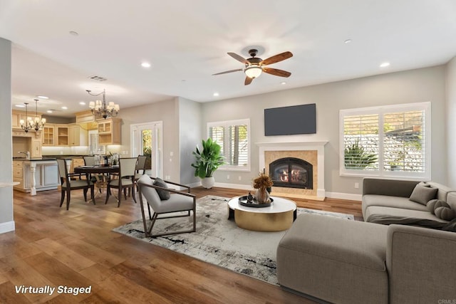 living room featuring hardwood / wood-style floors, ceiling fan with notable chandelier, a healthy amount of sunlight, and a tiled fireplace