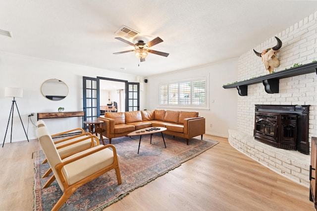 living room featuring french doors, a fireplace, light hardwood / wood-style floors, and ceiling fan