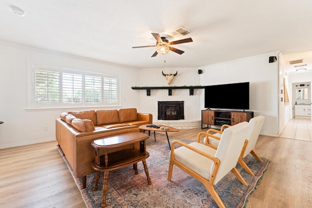 living room featuring ceiling fan, ornamental molding, a brick fireplace, and light wood-type flooring