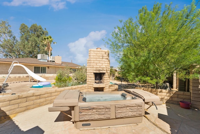 view of patio with a hot tub and an outdoor stone fireplace