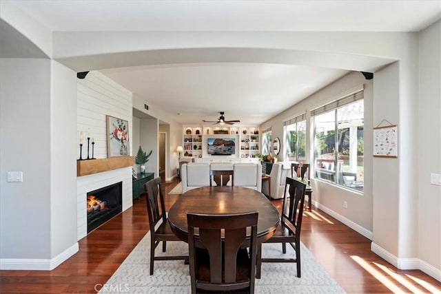 dining space featuring a large fireplace, arched walkways, wood finished floors, and baseboards