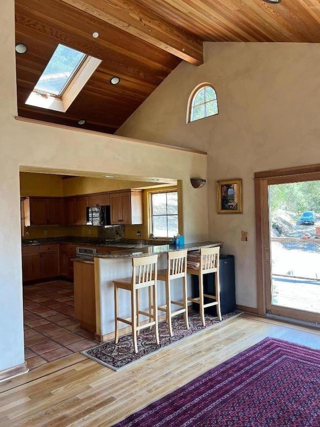 kitchen featuring a breakfast bar area, a skylight, wooden ceiling, kitchen peninsula, and beam ceiling