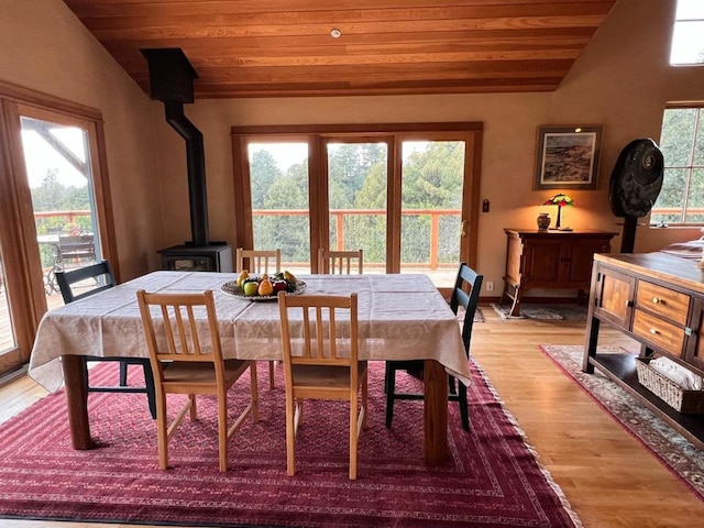 dining area with light wood-type flooring, wooden ceiling, vaulted ceiling, and a wood stove