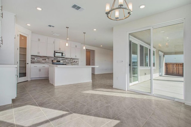 kitchen featuring white cabinets, decorative light fixtures, an island with sink, and appliances with stainless steel finishes