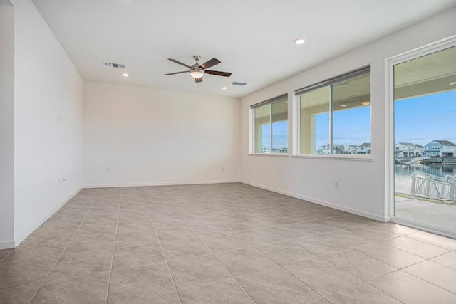 tiled spare room featuring ceiling fan and a water view