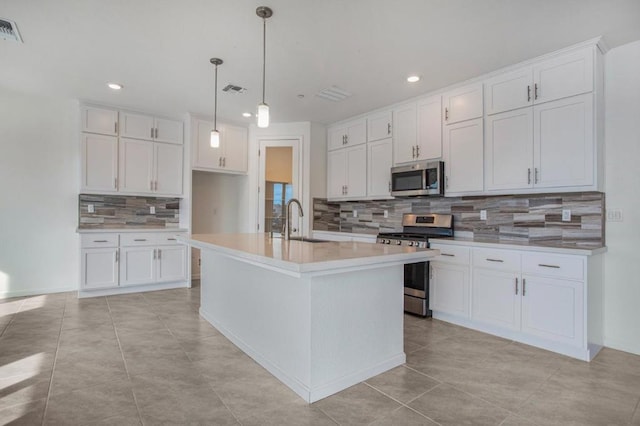 kitchen with backsplash, stainless steel appliances, white cabinetry, and a kitchen island with sink