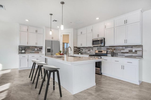 kitchen featuring a center island with sink, white cabinets, hanging light fixtures, and appliances with stainless steel finishes