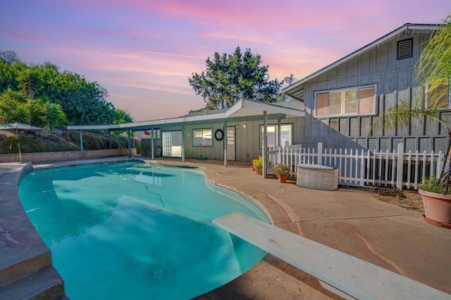 pool at dusk with a patio area and a diving board