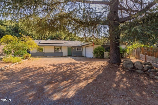 ranch-style home featuring a garage, roof mounted solar panels, and fence