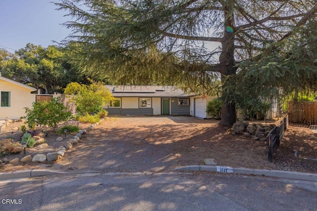 ranch-style house with fence, an attached garage, and solar panels