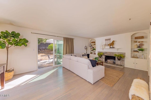 living area with built in shelves, a fireplace with raised hearth, and wood finished floors