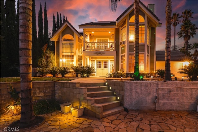 back house at dusk with french doors, a balcony, and a patio