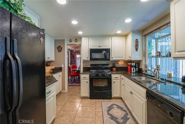 kitchen with sink, white cabinetry, black appliances, light tile patterned floors, and dark stone countertops