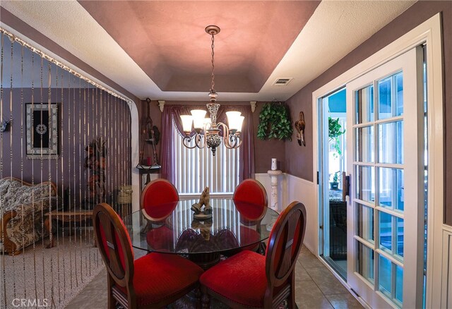 tiled dining room with a raised ceiling and a chandelier