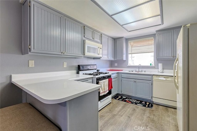 kitchen featuring light wood-type flooring, gray cabinets, a peninsula, white appliances, and a sink