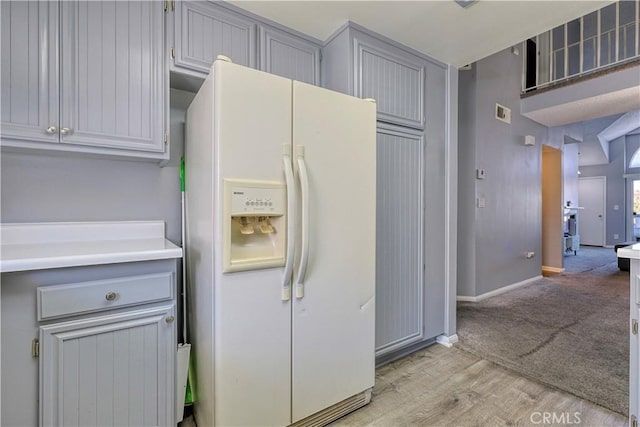 kitchen with baseboards, light wood-type flooring, light countertops, gray cabinets, and white refrigerator with ice dispenser