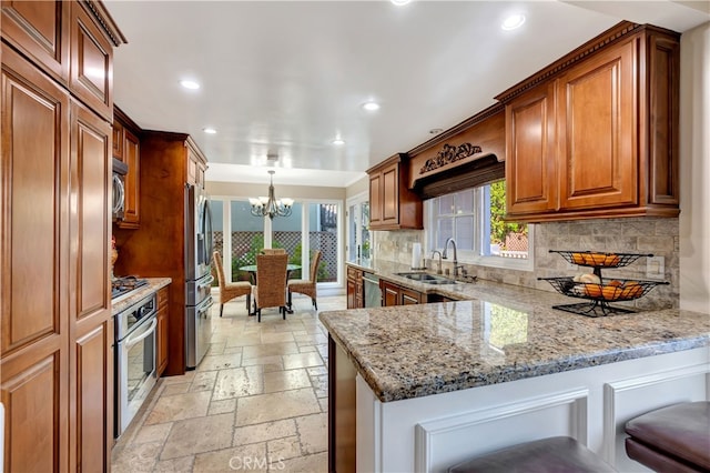 kitchen with pendant lighting, sink, tasteful backsplash, stainless steel appliances, and light stone countertops